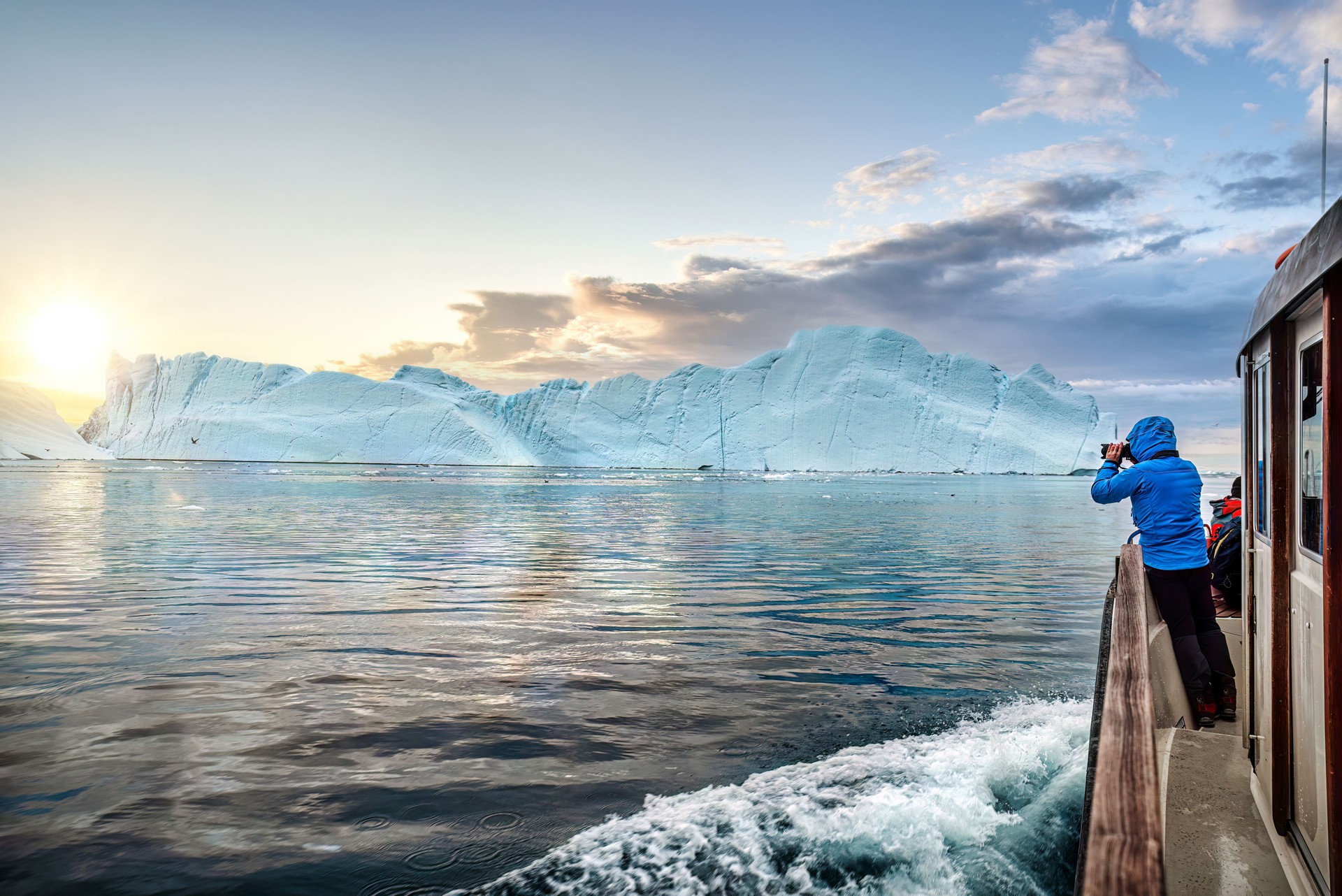 Travel in arctic landscape nature with icebergs,  tourist man explorer from a boat at sunset. Greenland