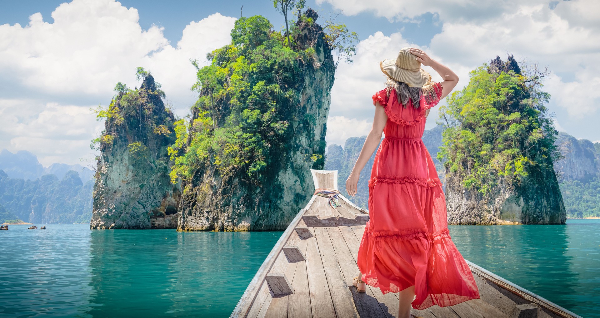 A famous cliffs and islands of Thailand to advertise tours. A woman in a dress on a Thai longtail boat looks at the Three Rocks nature panorama on Cheo Lan Lake in Khao Sok Park.